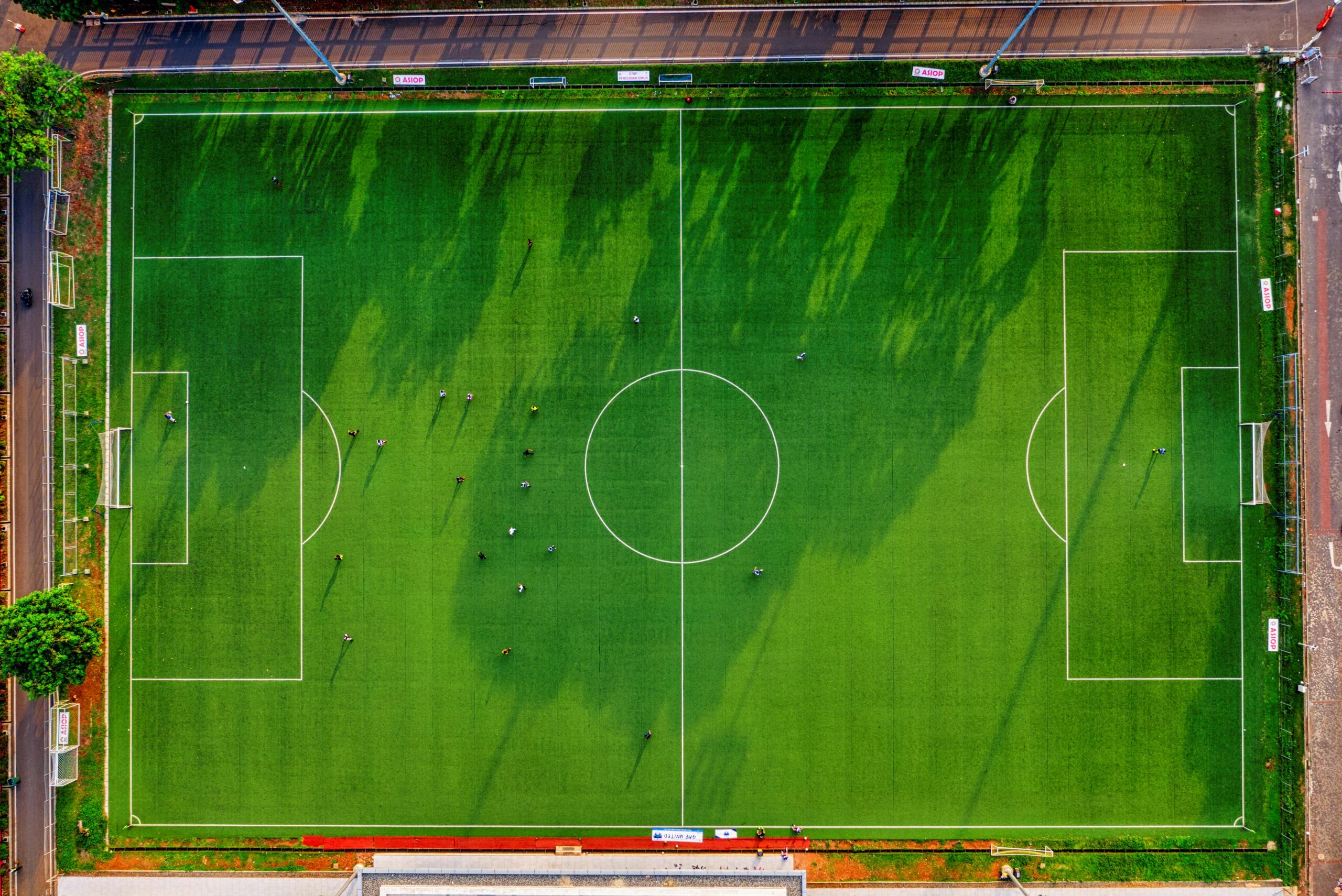 High-angle drone shot of a soccer field with players in Jakarta, Indonesia.