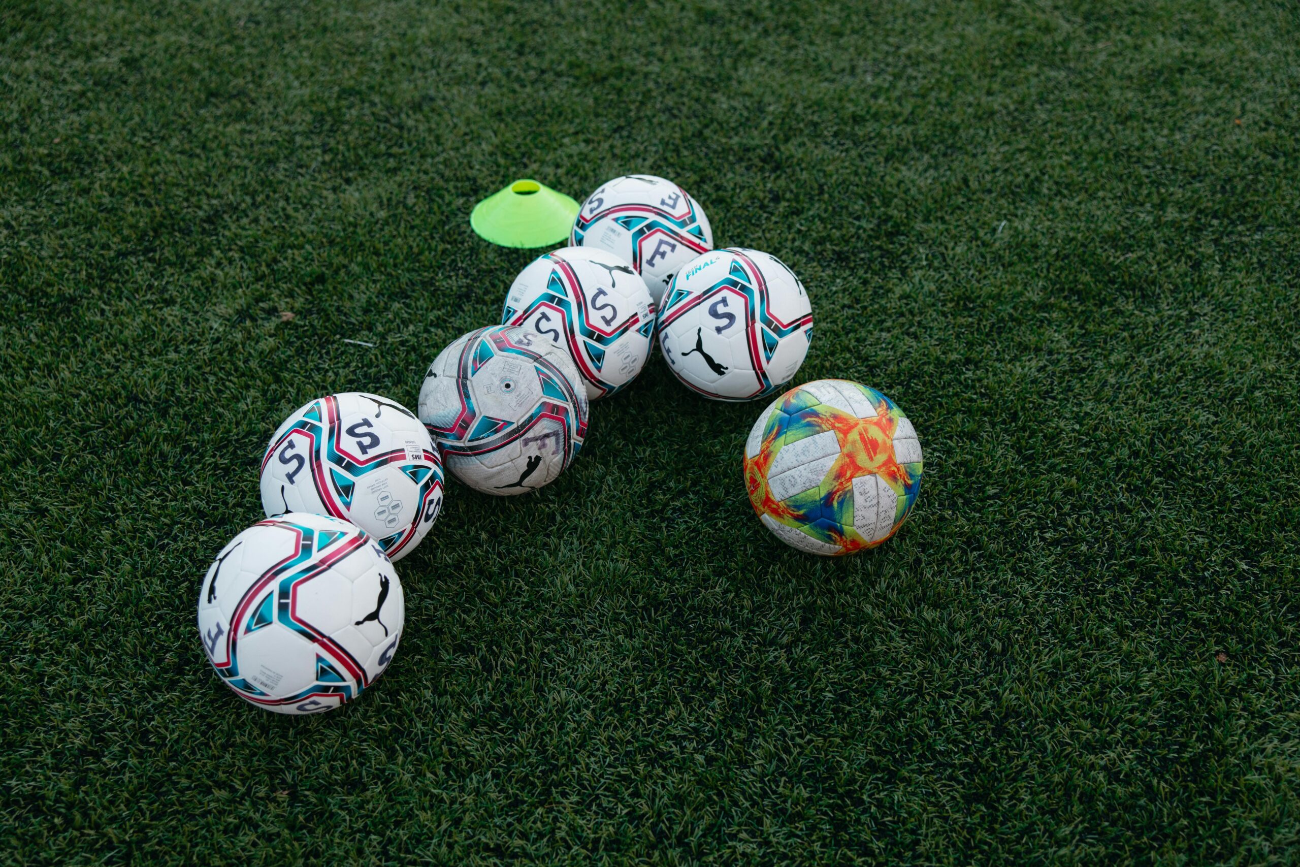 Group of soccer balls on a green grass field with a training cone, perfect for sports themes.